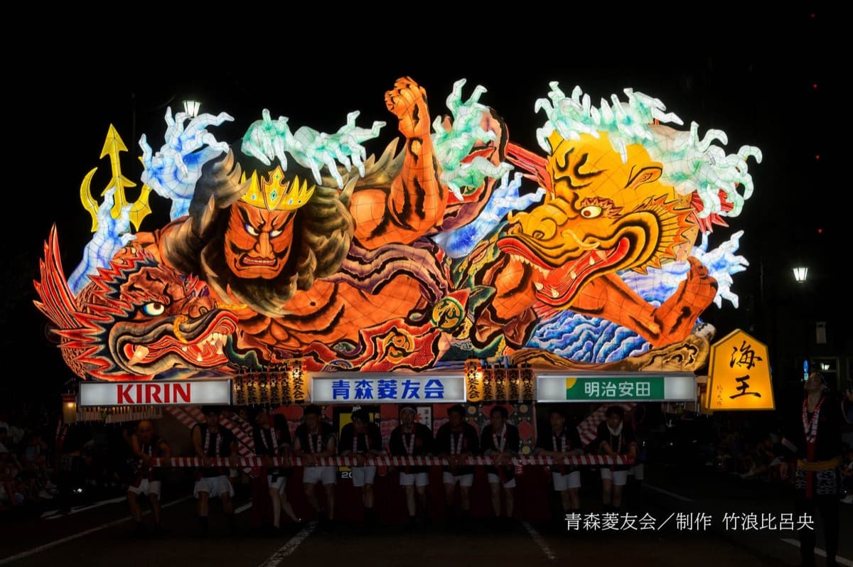 A giant illuminated Nebuta float depicting a sea king and dragon, hauled through the streets of Aomori by its hikite team at night