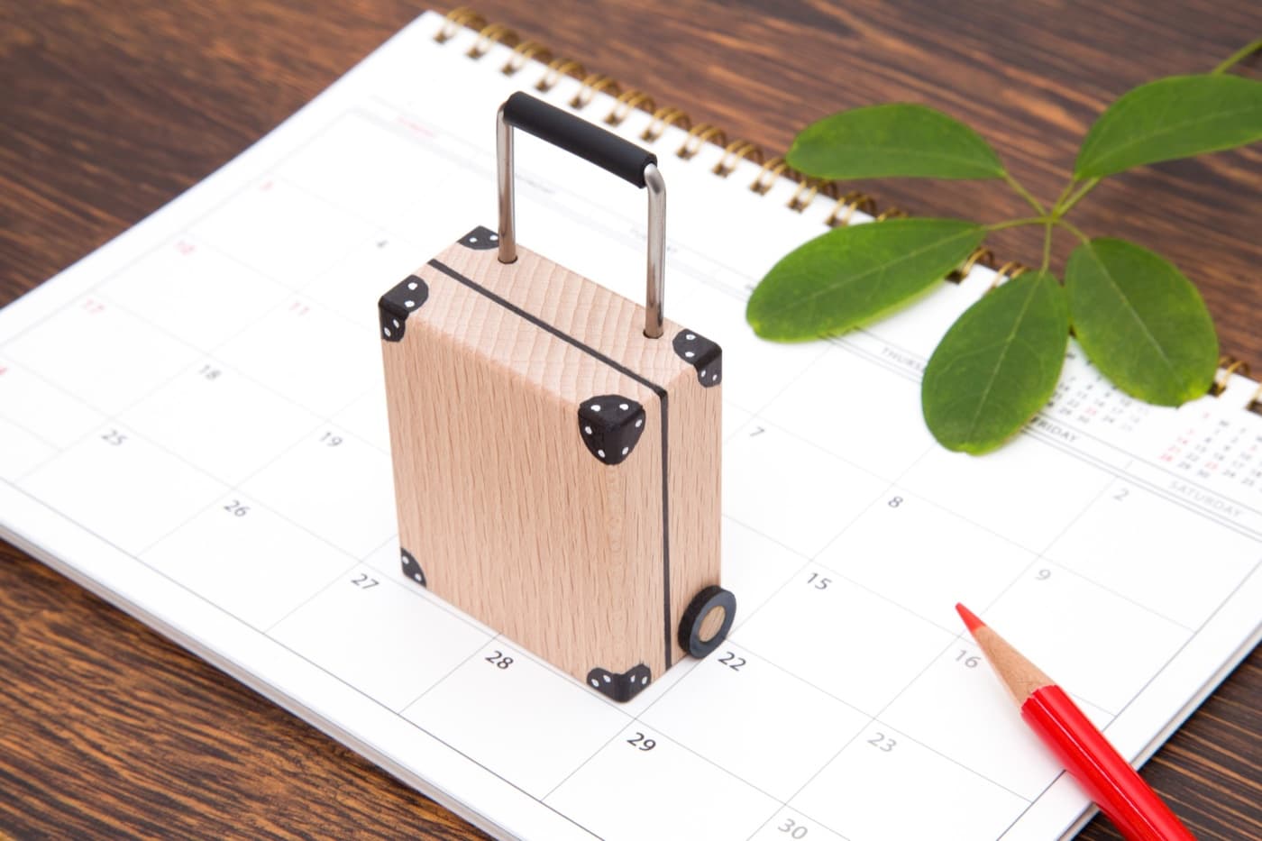 A miniature wooden suitcase standing on a desk calendar, symbolising fixing travel dates before booking a Golden Week trip