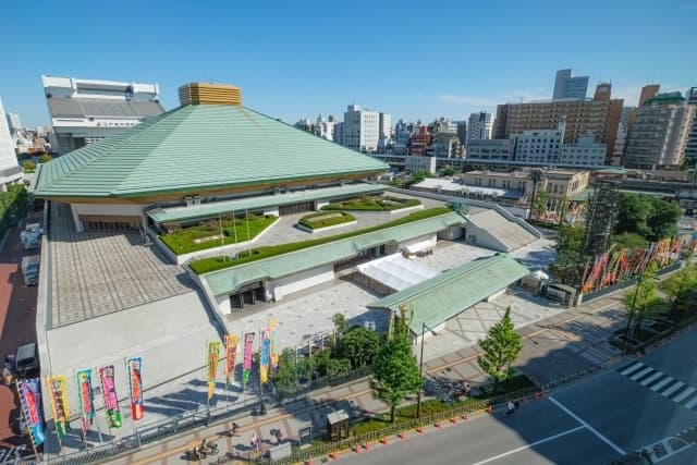 The Ryogoku Kokugikan sumo arena in Sumida-ku, Tokyo, seen from above with its green roof and rows of colourful banners along the street
