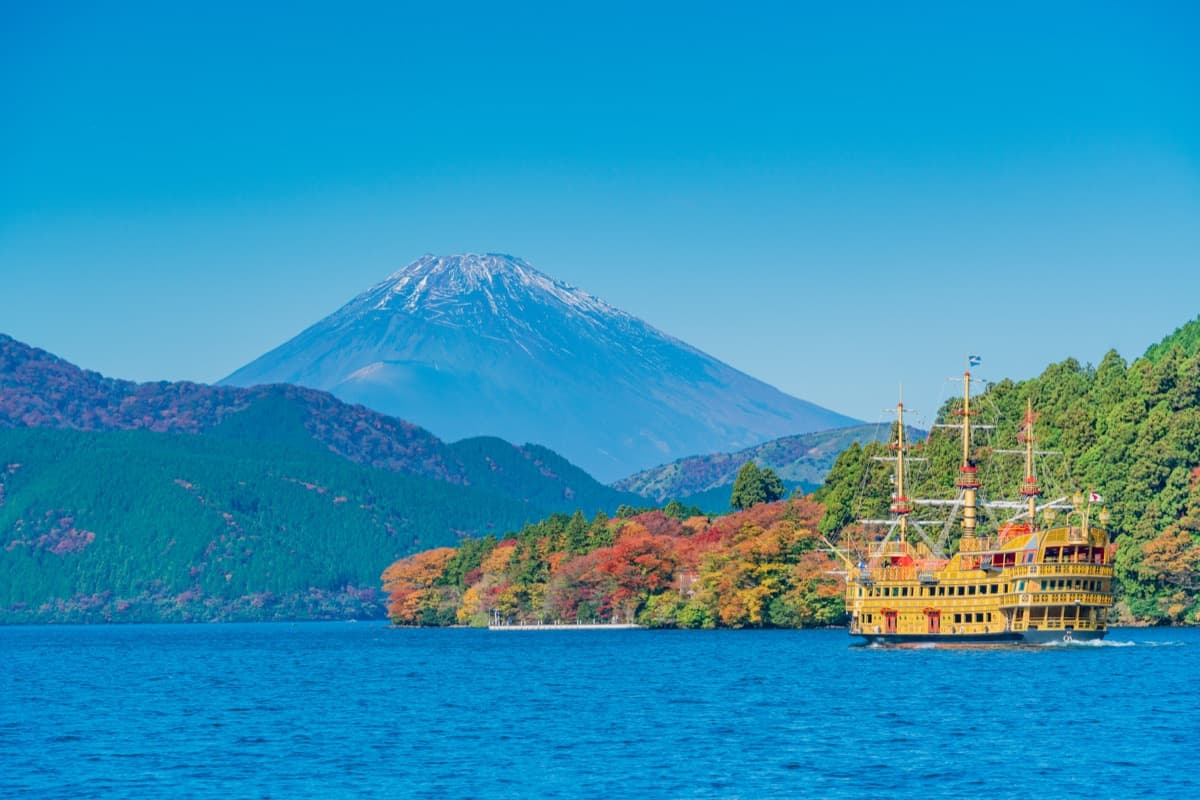 A pirate ship sailing on Lake Ashi past autumn trees, with snow-capped Mount Fuji behind the hills