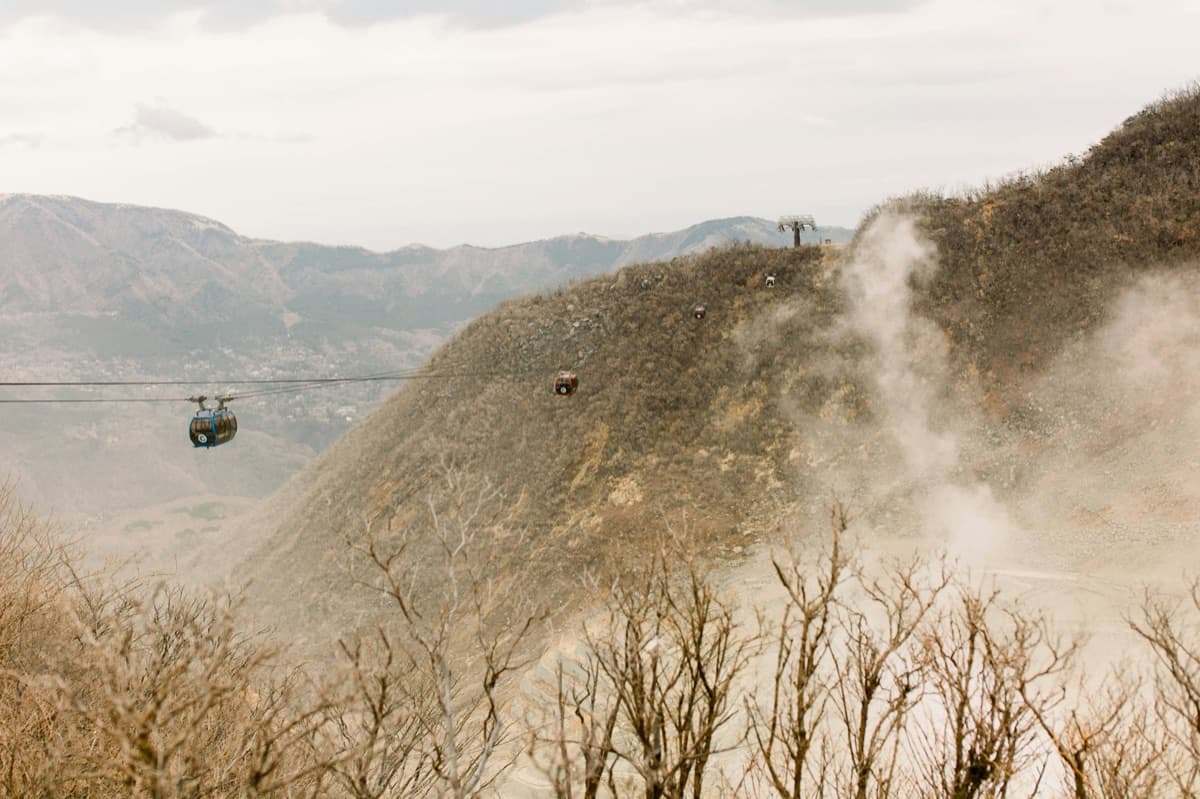 A Hakone Ropeway gondola passing above bare, steaming volcanic slopes at Owakudani