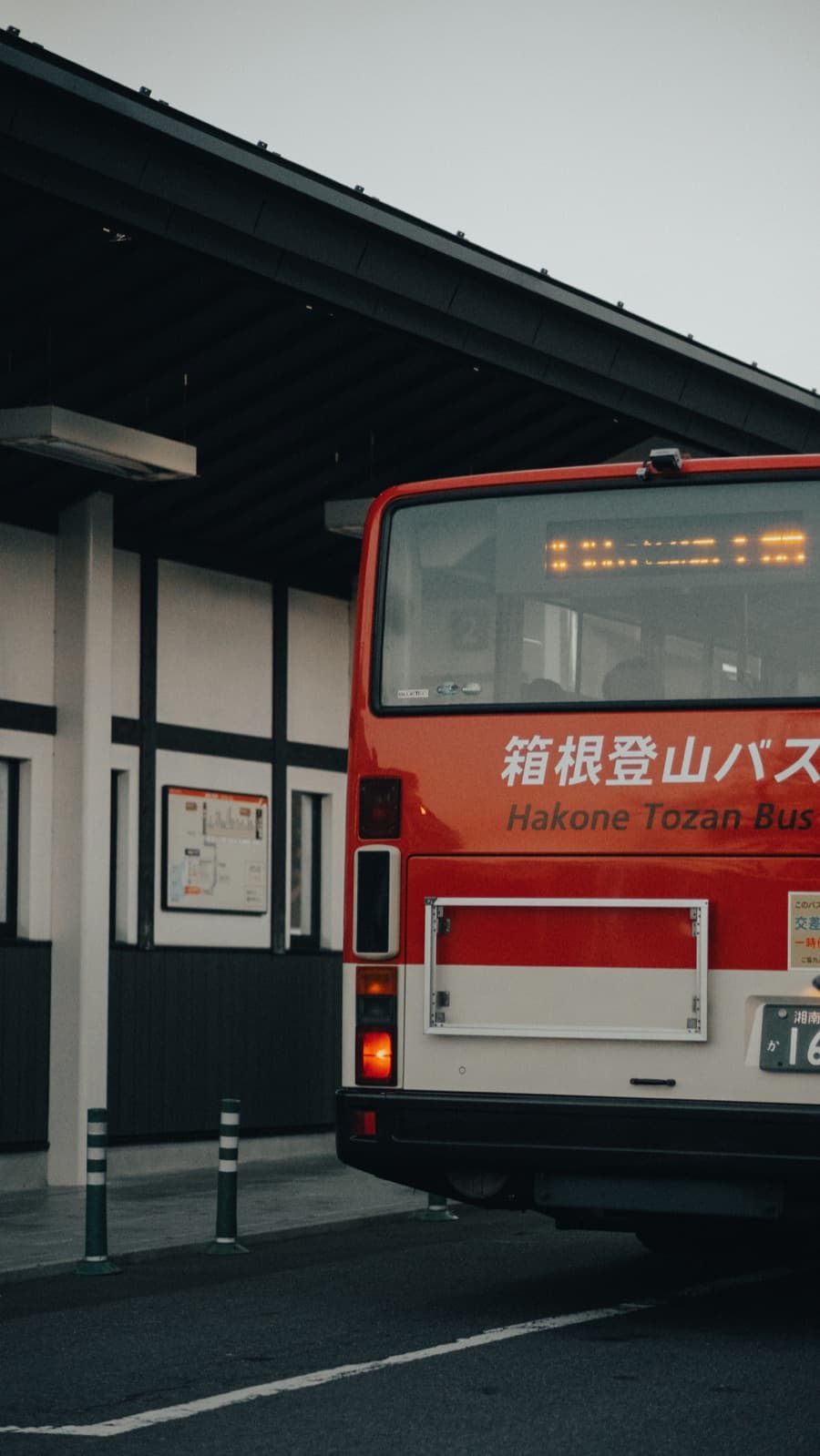 A red Hakone Tozan bus parked at a bus station with its destination sign lit