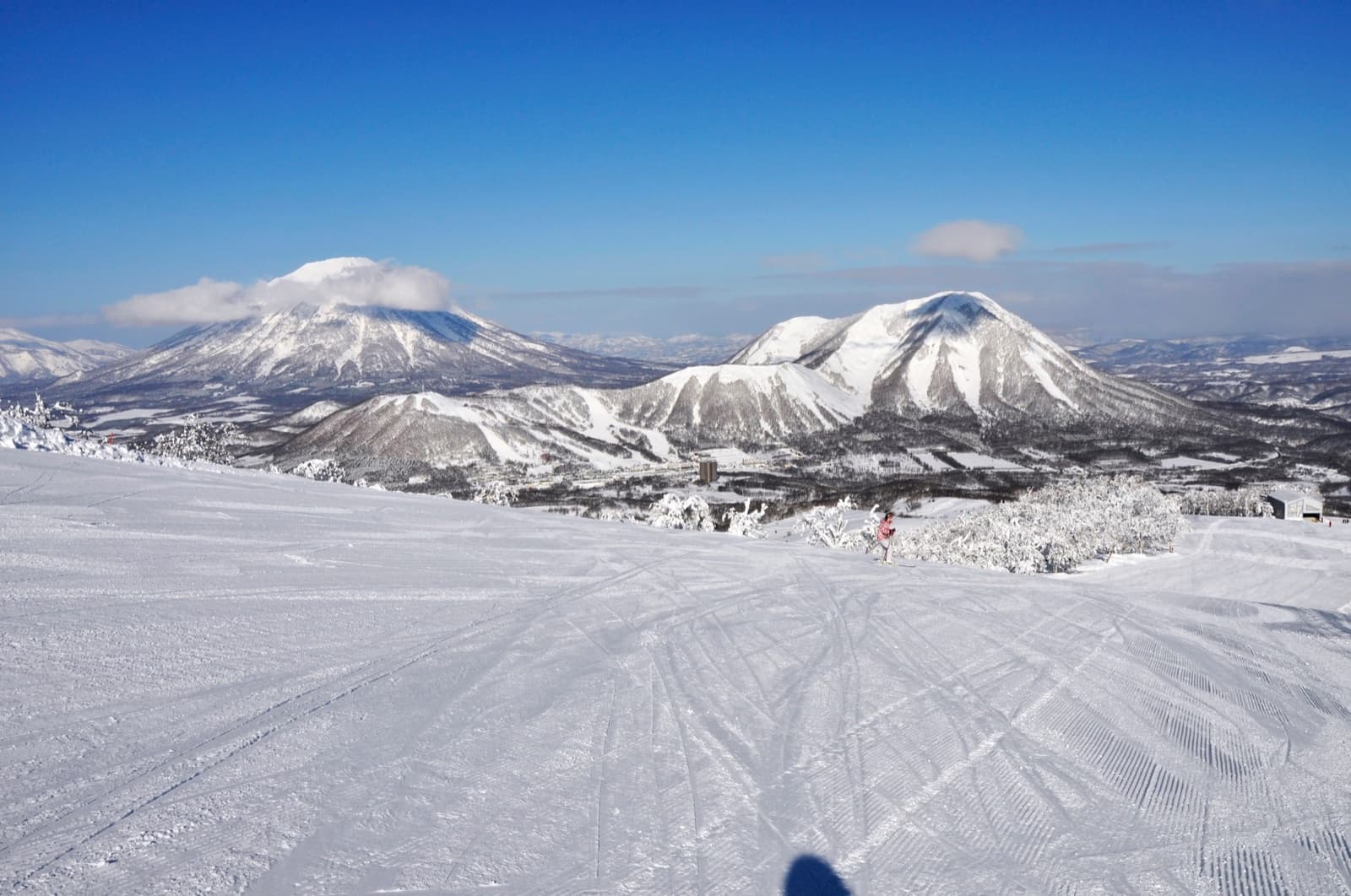 A wide groomed run at Rusutsu with snow-covered mountains on the horizon under a blue sky
