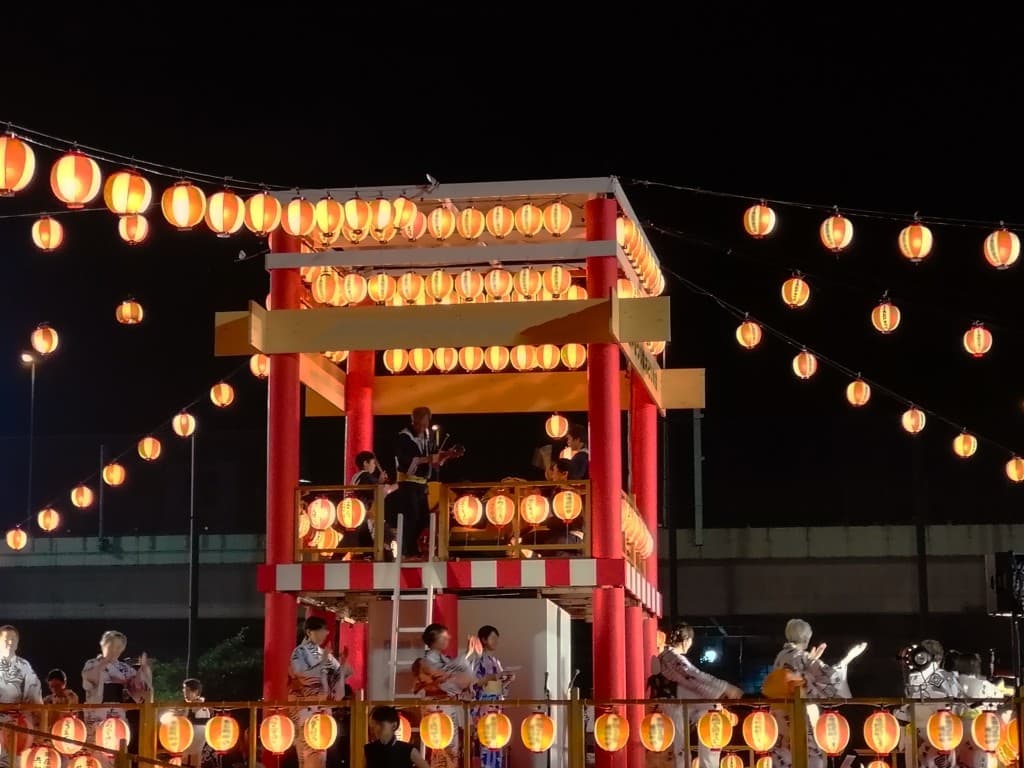 Dancers in yukata circling a lantern-lit yagura tower at a Tokyo bon odori festival