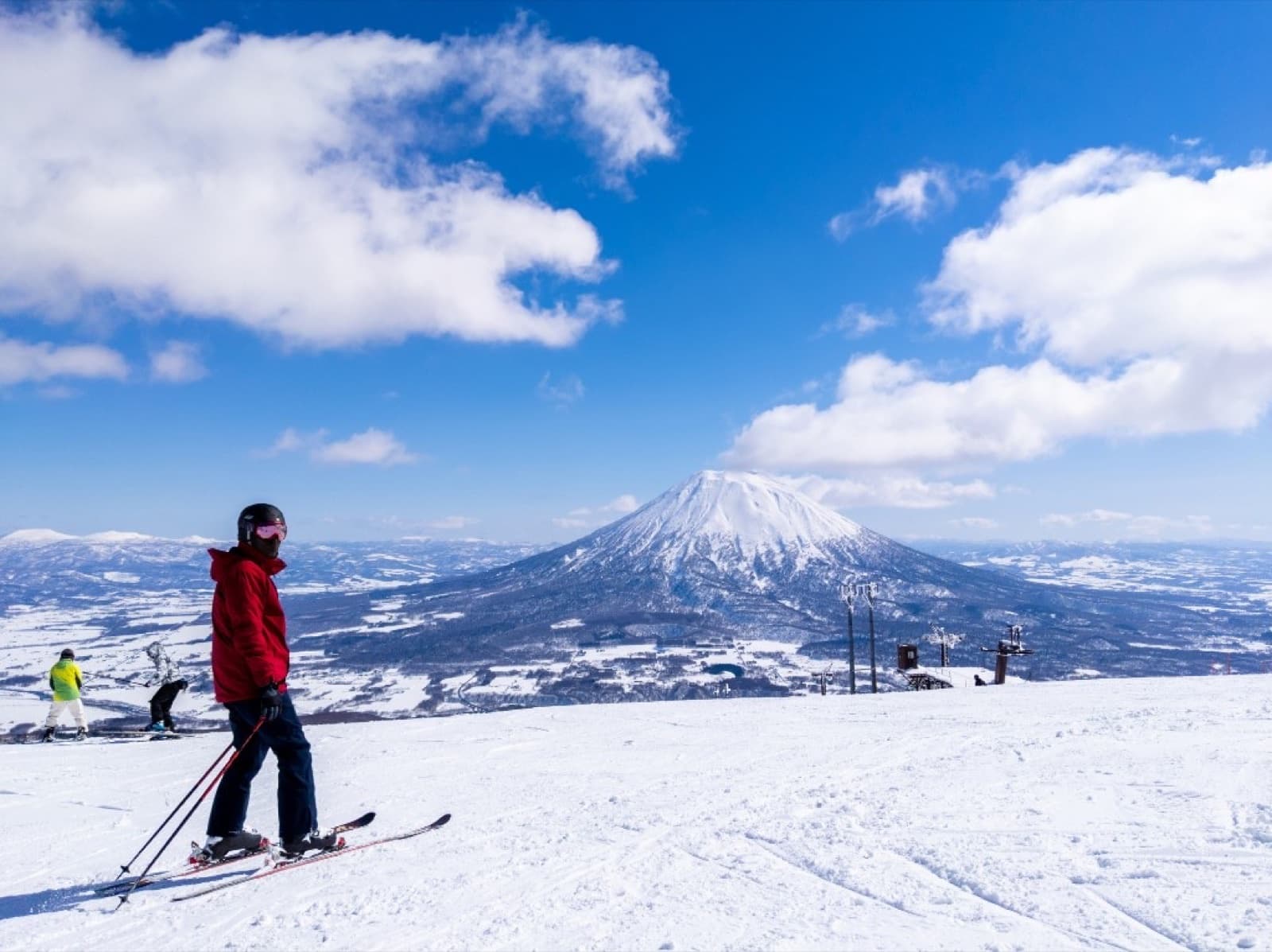Skier on a groomed run with Mount Yotei and blue sky in the background at Niseko