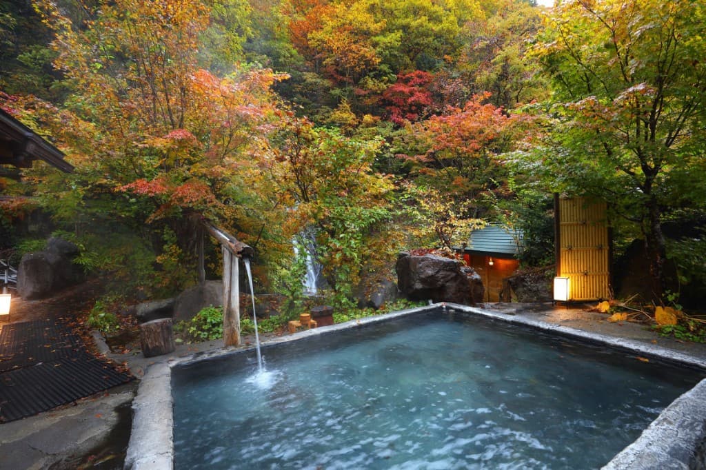 Outdoor onsen bath at a Japanese ryokan surrounded by autumn foliage