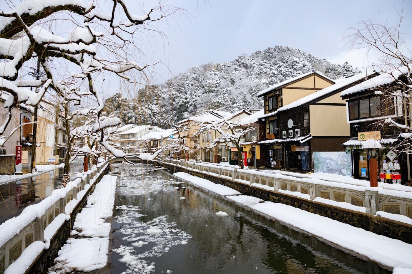 The Otani River canal in Kinosaki Onsen under snow, willow branches and the stone balustrades along both banks covered in white