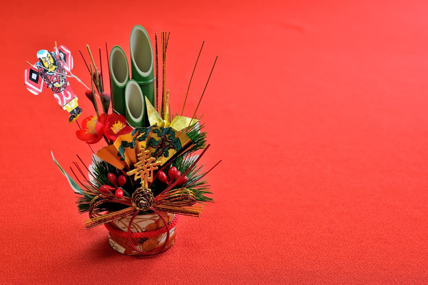 A miniature kadomatsu New Year decoration of pine, bamboo and plum against a red background