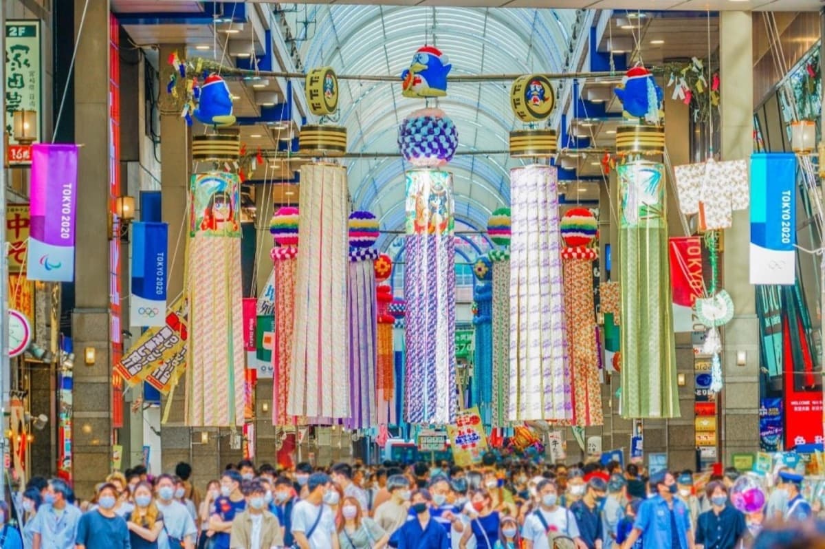 Crowds walking beneath massive Tanabata fukinagashi streamers in a covered shopping arcade in Sendai