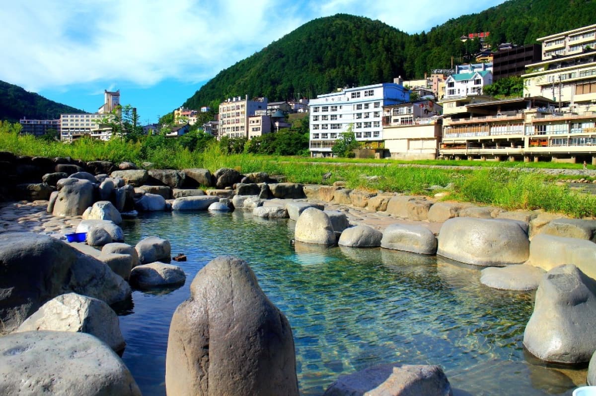 The riverside Funsenchi open-air hot spring bath at Gero Onsen with mountain-backed ryokan in the background
