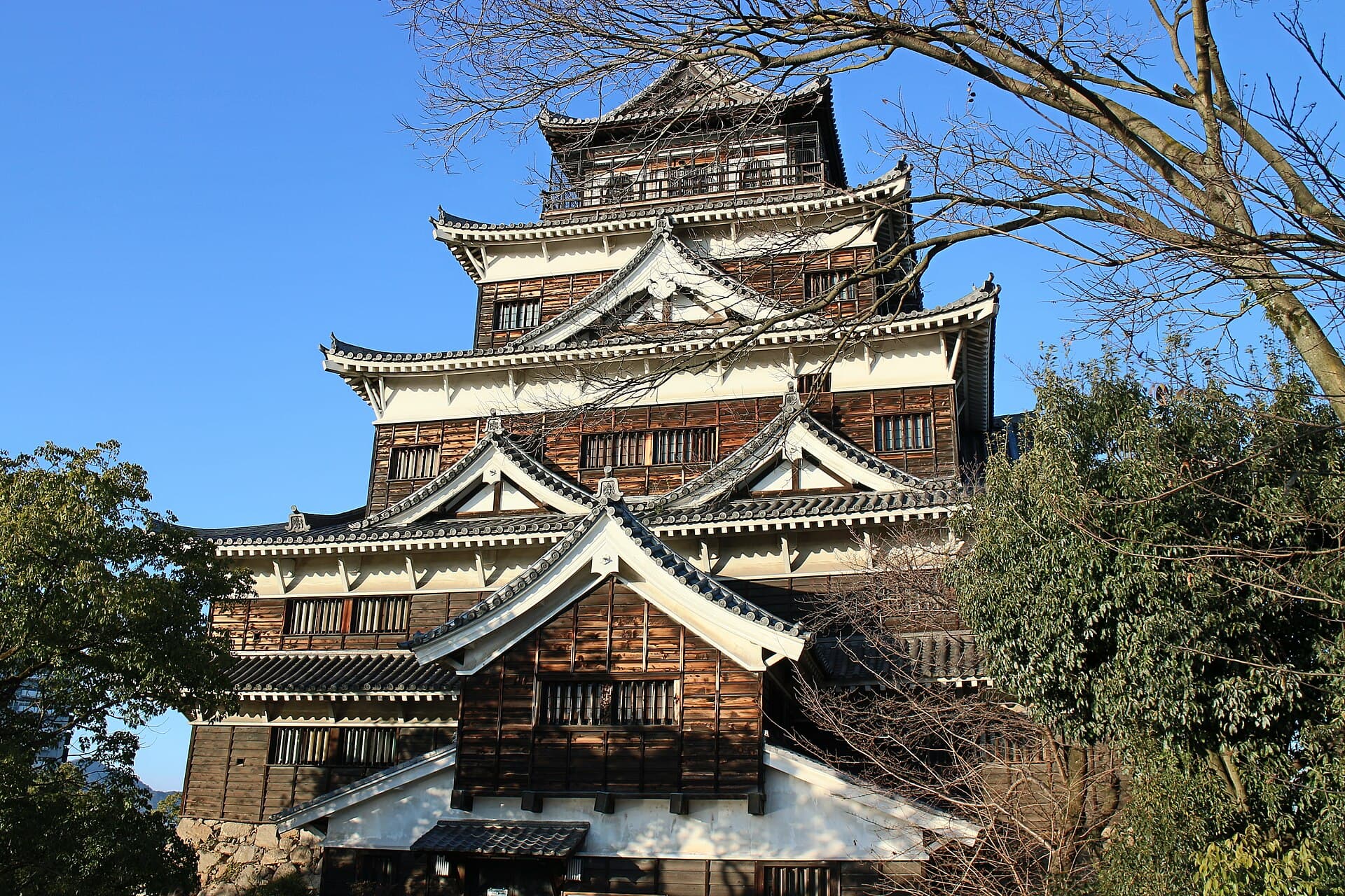 Hiroshima Castle's five-story black-and-white keep rising above trees against a clear blue sky