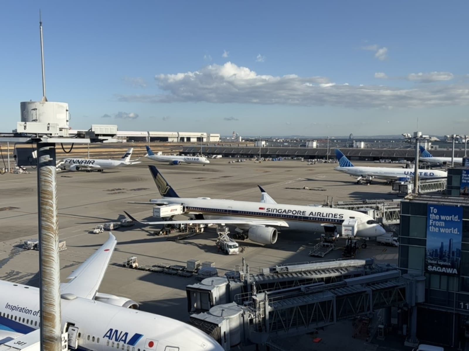 International aircraft parked at a busy Japanese airport tarmac with ground service vehicles