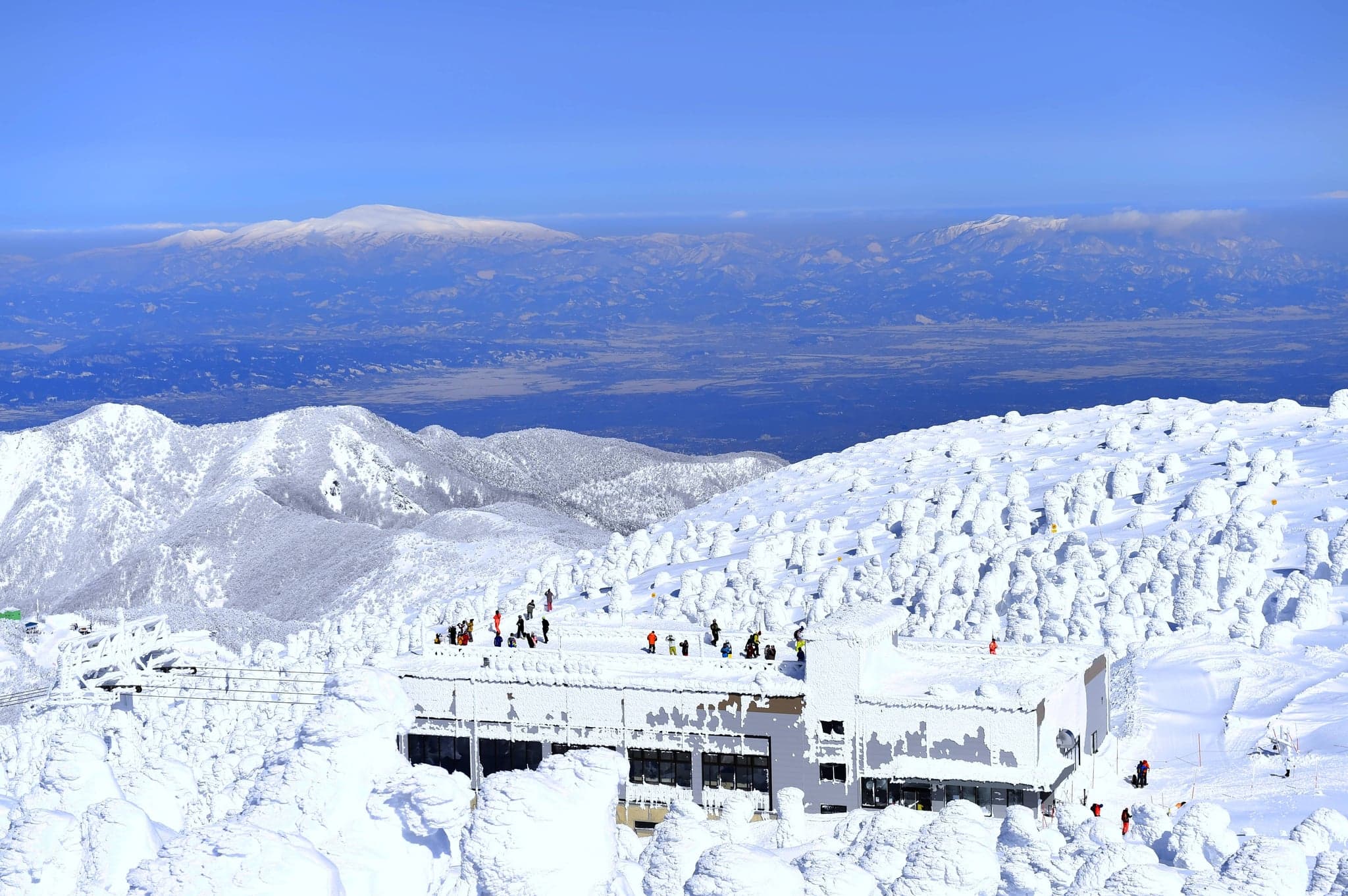 Snow monsters, rime-covered fir trees, around the ropeway summit station at Zao Onsen with mountains in the distance