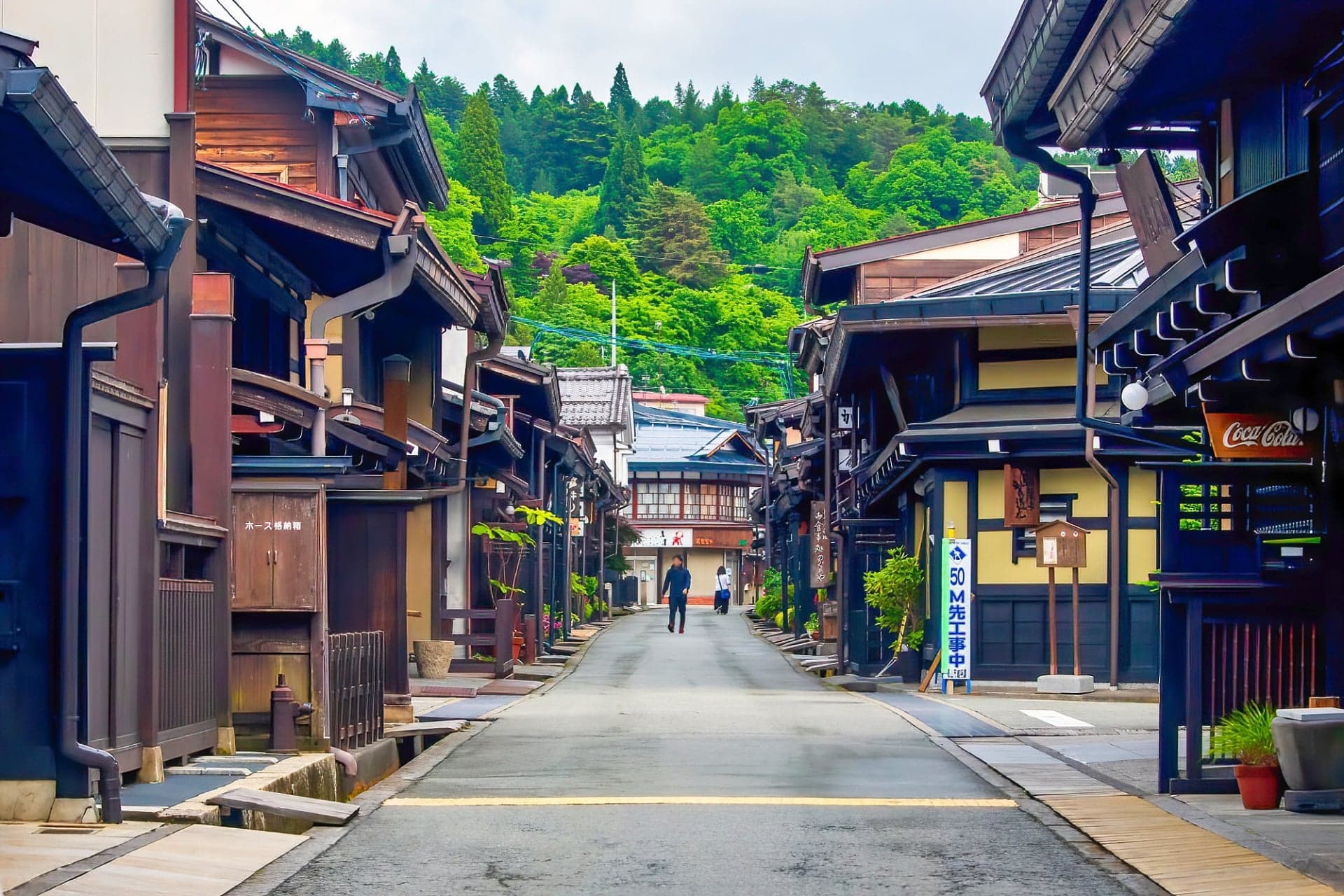 A quiet street of preserved wooden merchant houses in Takayama’s old town with forested hills behind