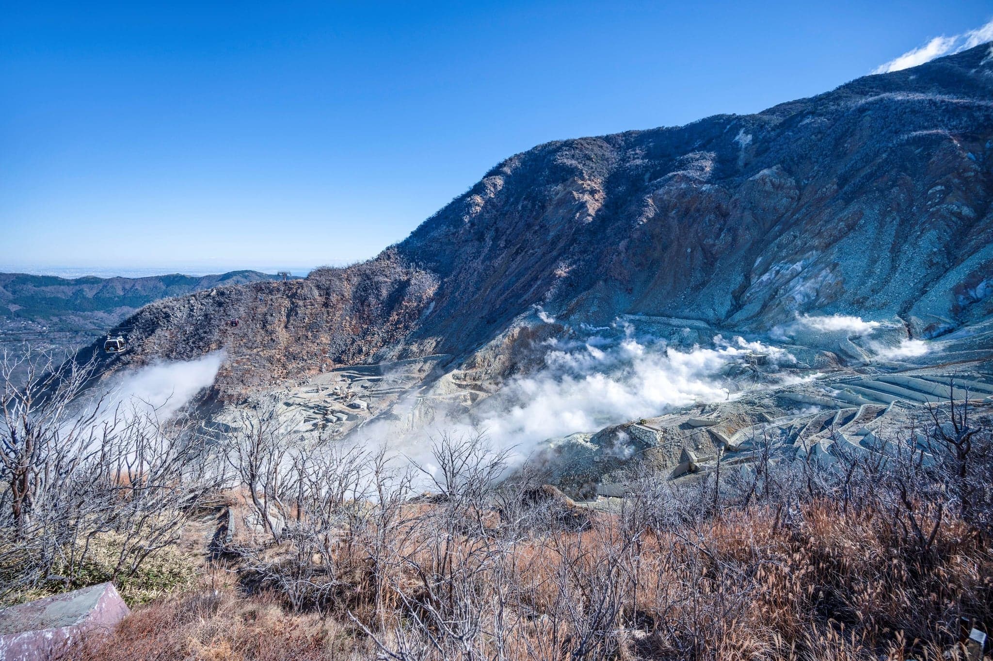 Steam rising from grey volcanic slopes at Owakudani in Hakone under a blue sky