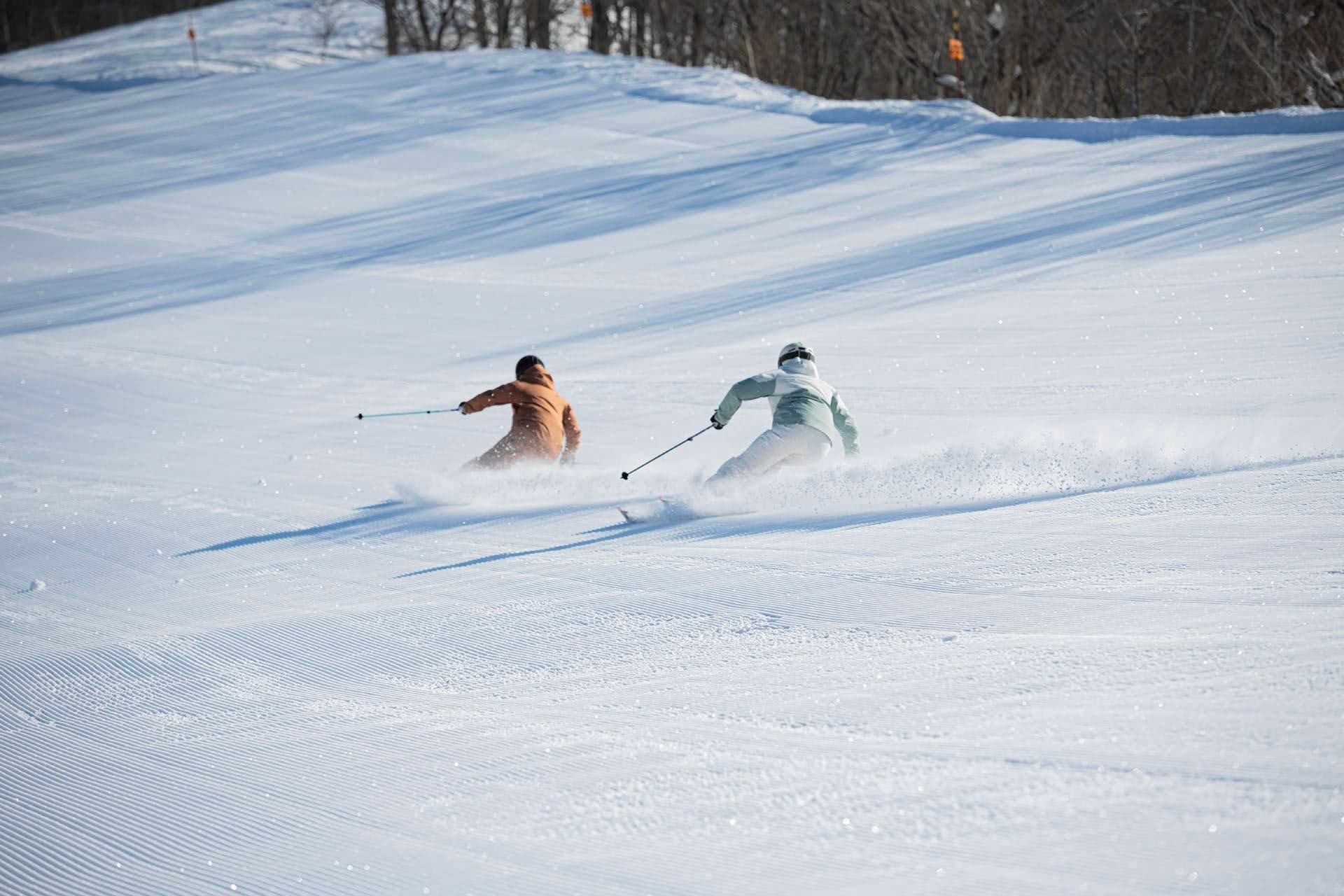 Skiers on a wide, freshly groomed run in Hakuba with snow-covered forest on both sides
