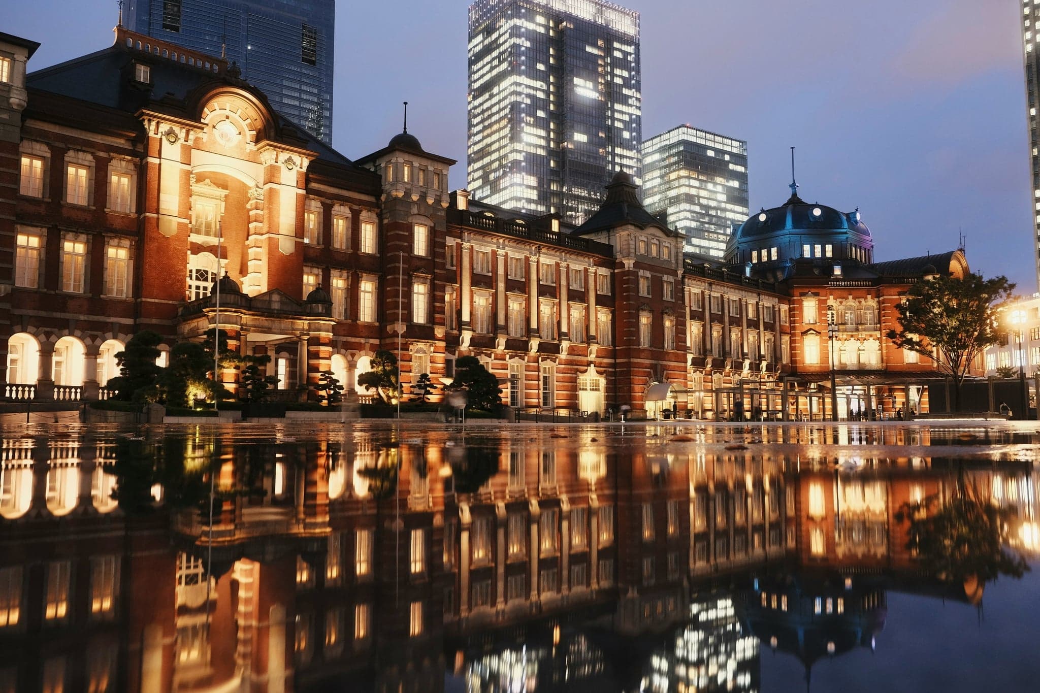 Tokyo Station's red-brick Marunouchi building lit up at night and reflected in the plaza