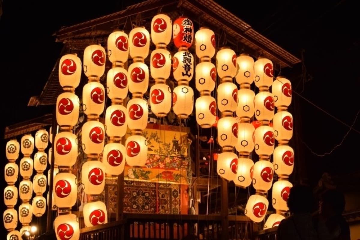 A Gion Matsuri float illuminated by hundreds of chochin lanterns during Yoiyama night, with the Kita Kannon-yama goshinto lantern visible