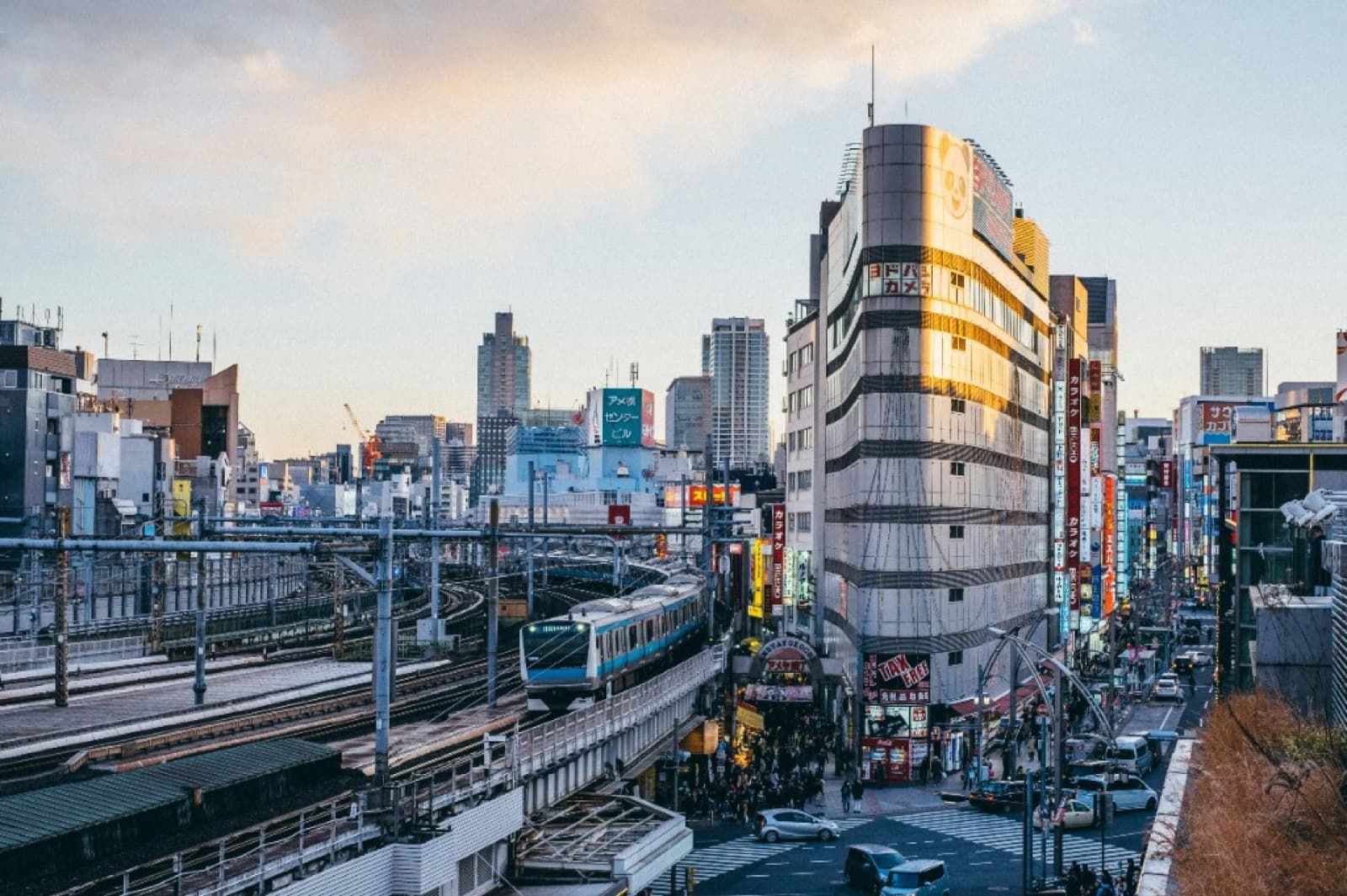A commuter train passing through central Tokyo near Okachimachi at dusk, with shops and crowds below