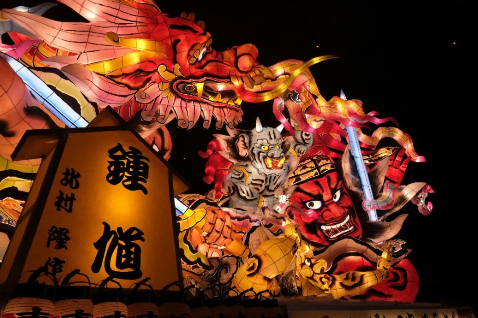 Dragon-shaped Aomori Nebuta float made of painted washi paper over a wire frame, lit at night