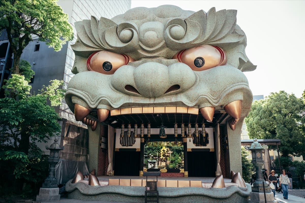 The giant lion-head stage of Namba Yasaka Shrine with its open mouth, stone lanterns and trees around it
