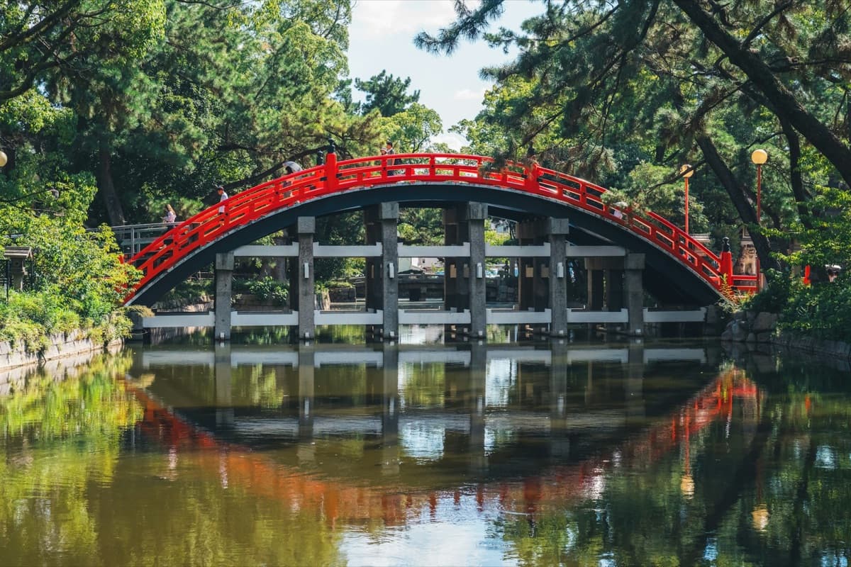 The red arched Sorihashi bridge at Sumiyoshi Taisha reflected in the still pond among trees