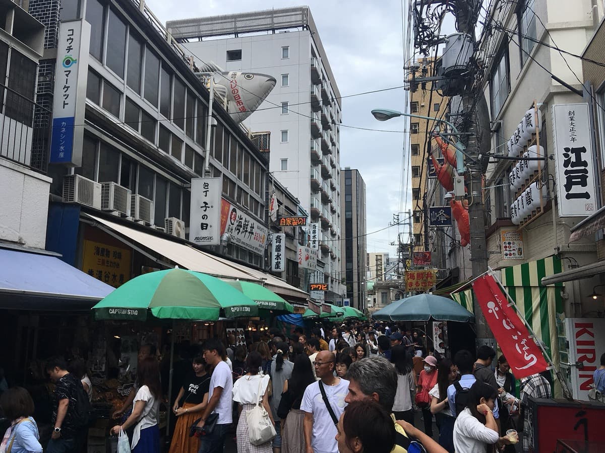 Crowds of people in a narrow lane lined with food stalls at the Tsukiji Outer Market