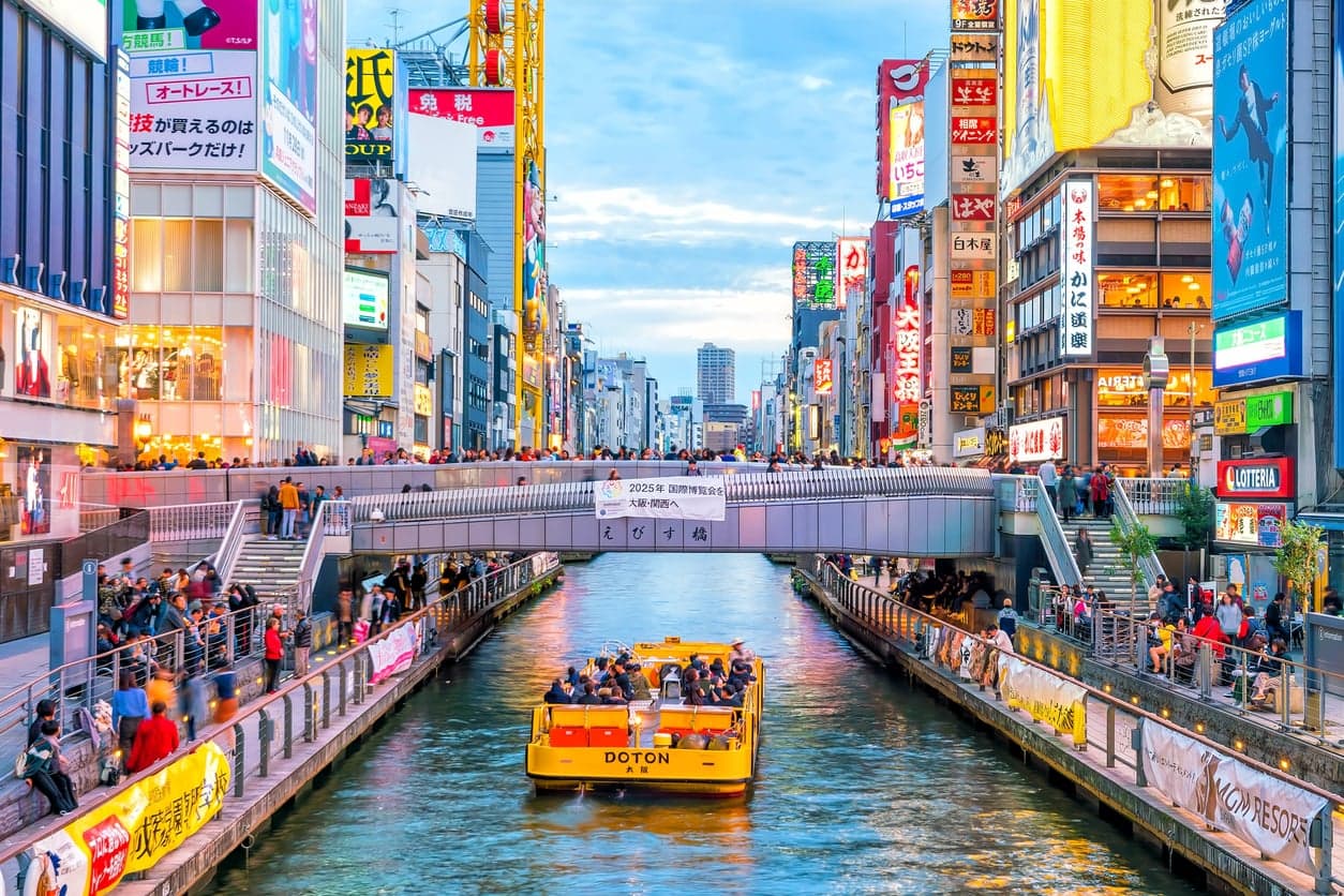 The Dotonbori canal in Osaka with a yellow river cruise boat and walkways lined with giant neon signs